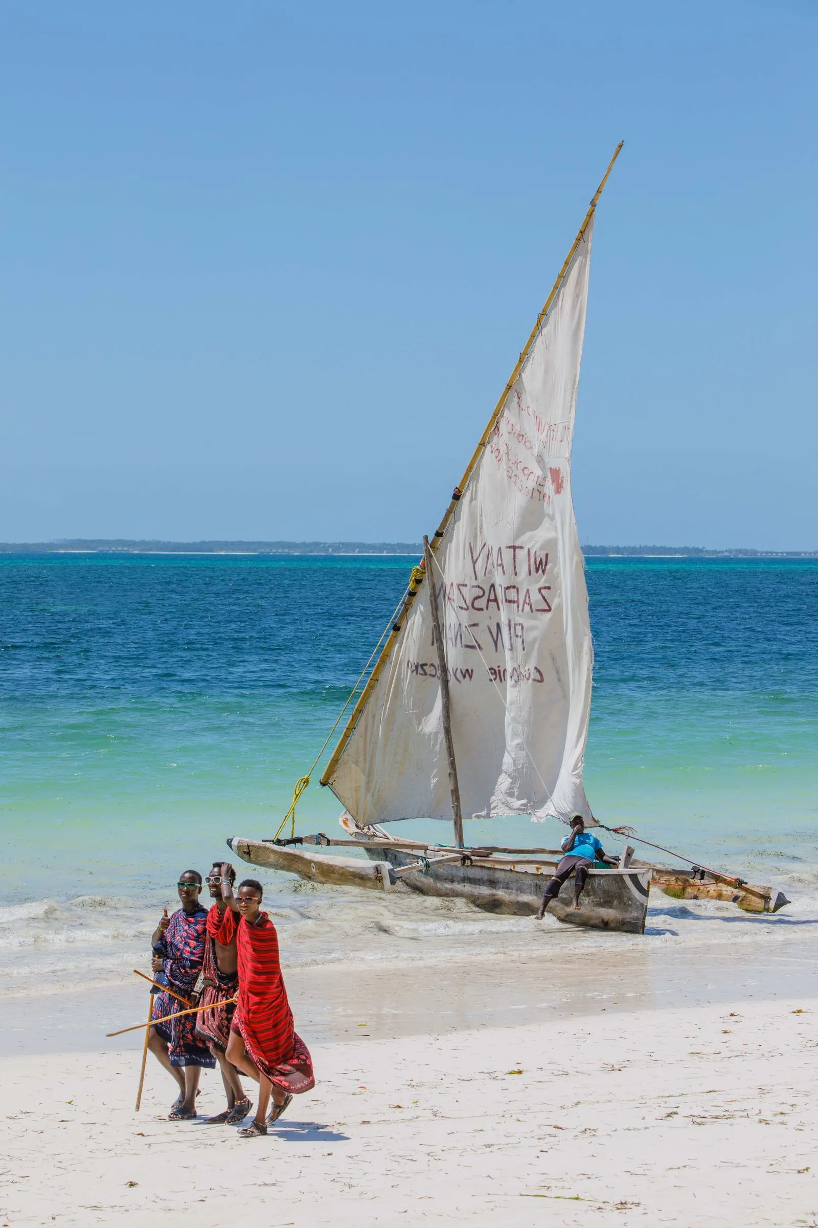 A traditional sailboat and people on a tropical beach